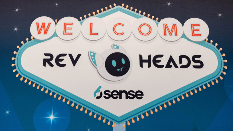 Las Vegas-style welcome sign for "REV HEADS" event by 6sense, featuring turquoise border and cartoon astronaut mascot.